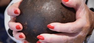 Handen met roodgelakte nagels omsluiten een kanonskogel