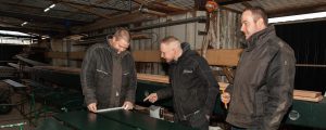 Drie molenmakers in opleiding meten lange groene planken op.