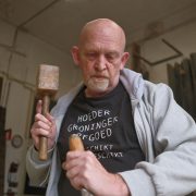 Een man is in een werkplaats iets met een houten hamer aan het bewerken.