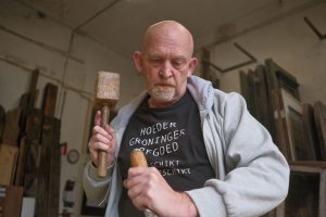 Een man is in een werkplaats iets met een houten hamer aan het bewerken.